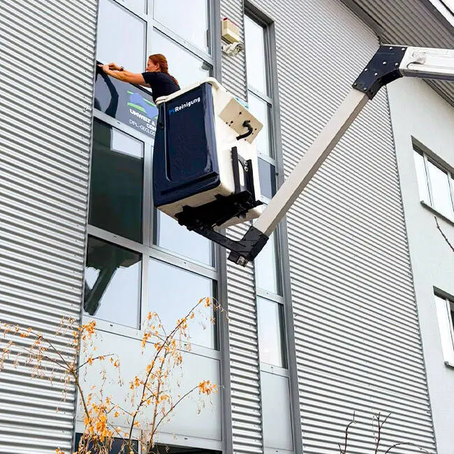 Monteurin bringt von der Hubarbeitsbühne aus ein Werbeschild an einer Fassade an