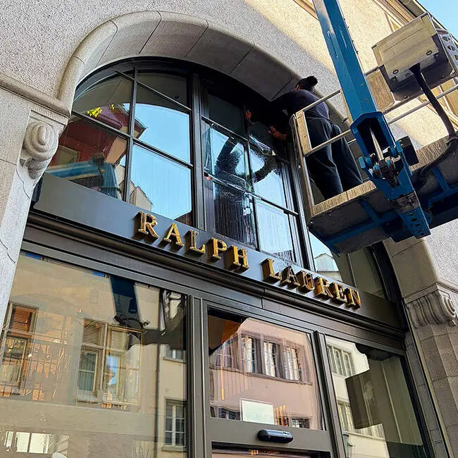 Montage von Sonnenschutzfolie an den Rundbogenfenstern des Ralph-Lauren-Stores von der Hubarbeitsbühne aus
