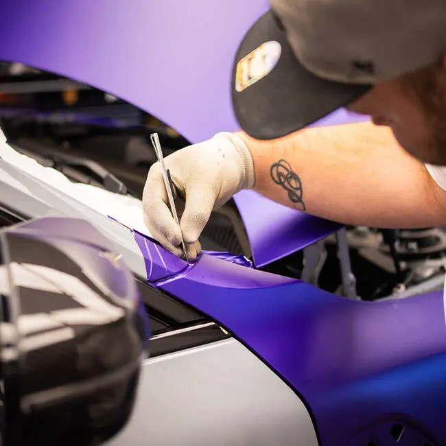 Monteur der Alpha Group zieht violette Folie über die Karosserie eines Fahrzeugs